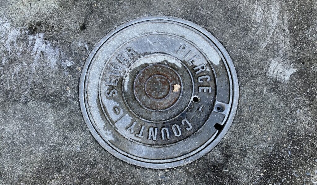 Close-up of metal manhole cover stamped "Pierce County Sewer" on pavement.