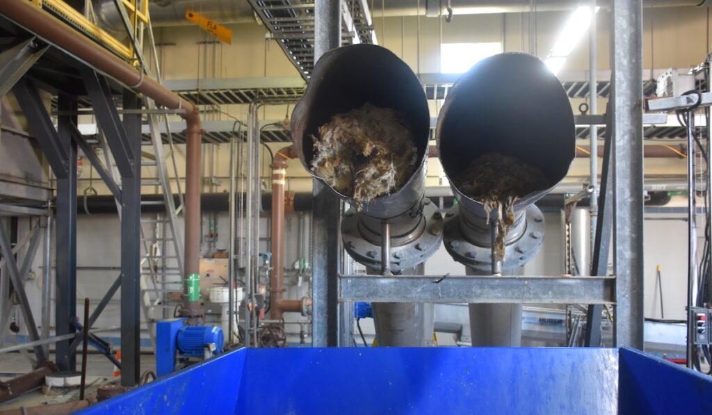 Two large pipes with screened solid material removed during preliminary wastewater treatment.