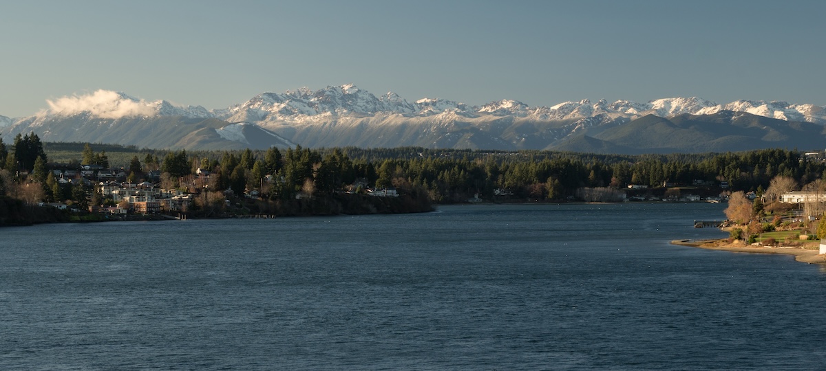 Waterfront view of Puget Sound with snow-capped Olympic Mountains in distance and residential shoreline in foreground
